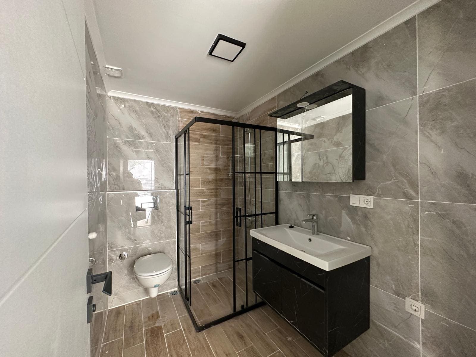 Siyah çerçeveli duşakabinli, mermer görünümlü seramik kaplı banyo