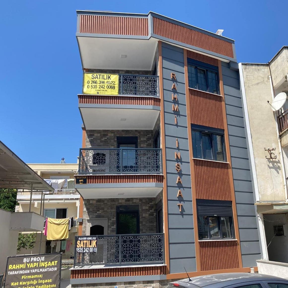 Cephesinde 'Rahmi İnşaat' yazan, gri ve ahşap görünümlü kaplamalı yeni apartman