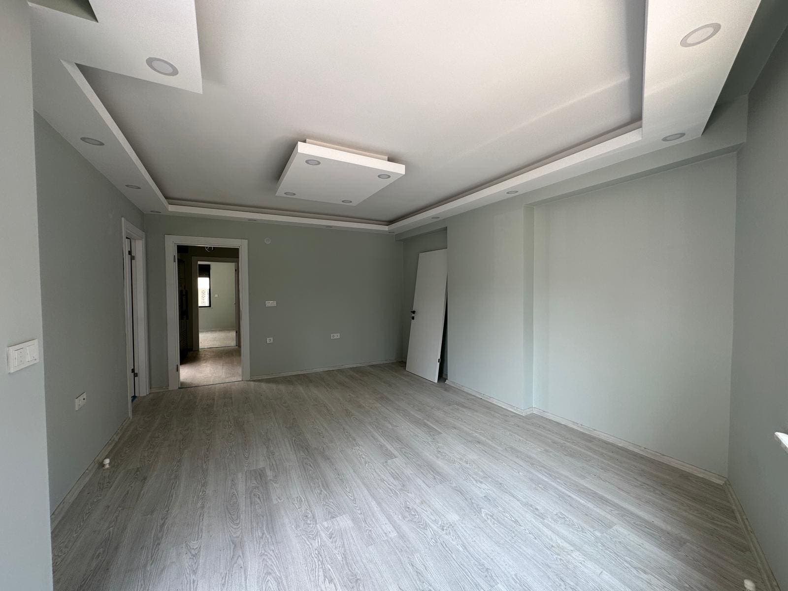 Asma tavan aydınlatmalı, ahşap görünümlü zeminli salon